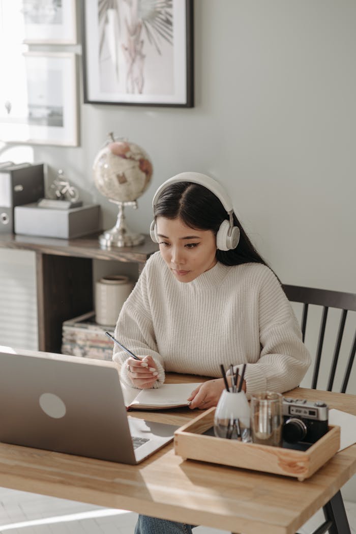 Woman wearing headphones focused on studying with laptop at home.